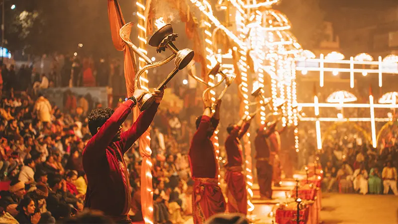 Priests performing a traditional evening ritual beside a crowded riverfront