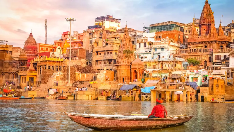 Panoramic view of a historic river city with temples, ghats, and traditional boats