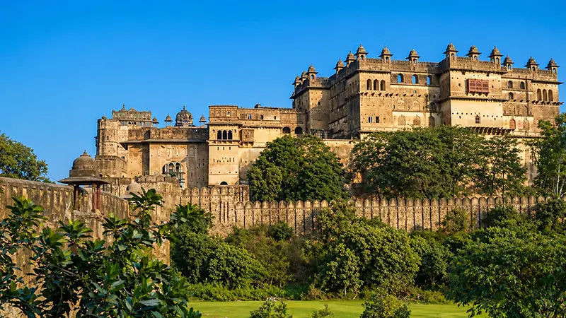 Massive hilltop citadel surrounded by fortified walls and lush greenery
