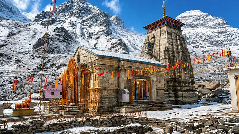 Stone Kedarnath temple decorated with flags and snow covered mountains behind