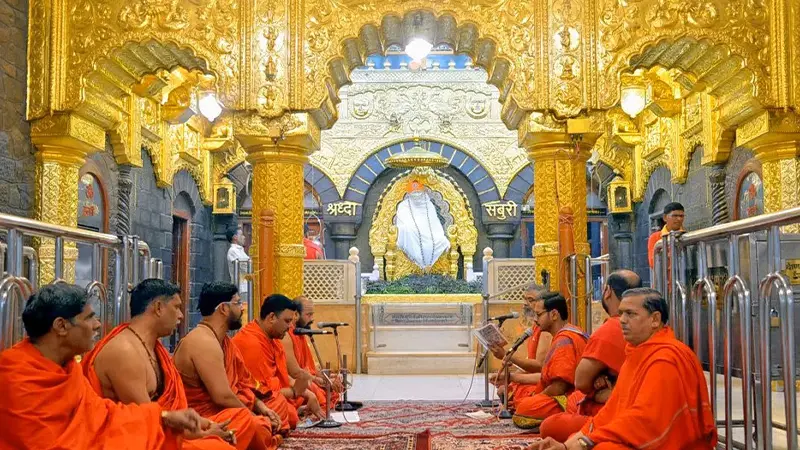 Priests performing devotional chants inside an ornate hall decorated with golden carvings