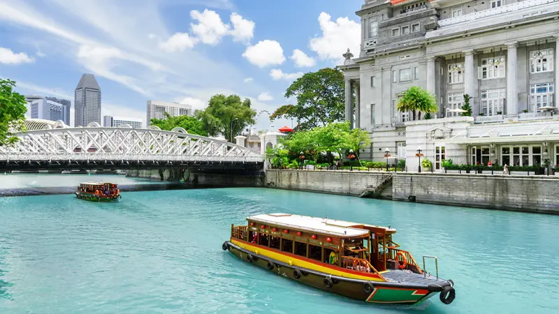 Traditional river cruise boat sailing along the Singapore River beside heritage landmarks