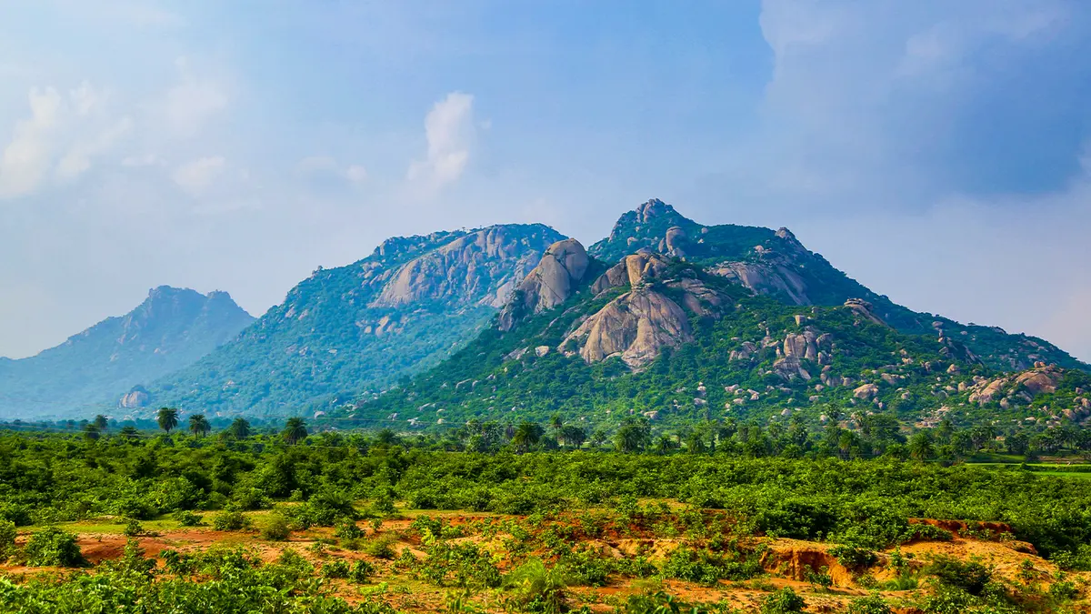 Scenic granite ridge rising above lush wilderness and open countryside