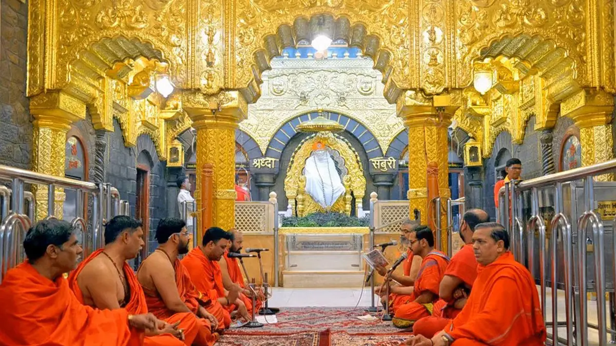 Priests performing devotional chants inside an ornate hall decorated with golden carvings