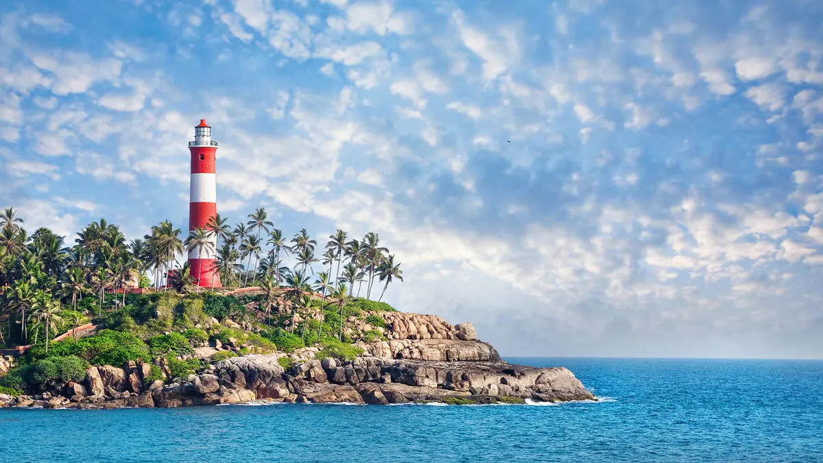 Red and white coastal beacon standing beside waves and rocky shoreline