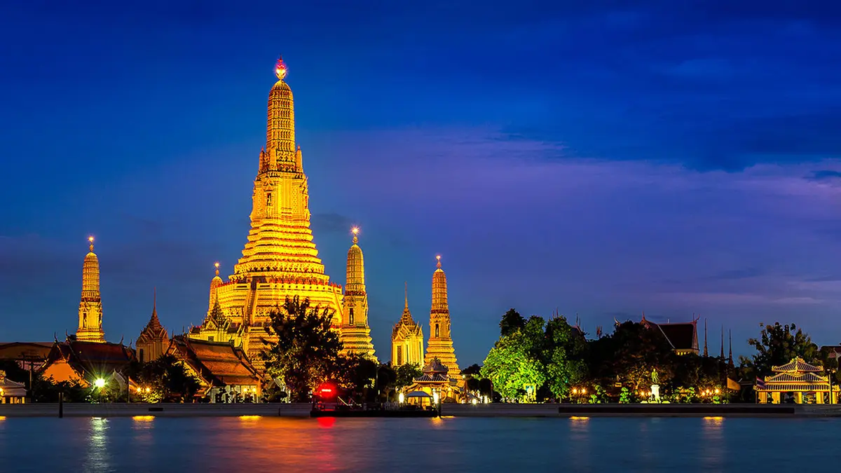 Illuminated Wat Arun Temple reflected on the Chao Phraya River at twilight in Bangkok